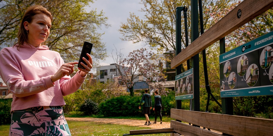 Vrouw kijkt op haar gsm aan de beweegbank Vrouw kijkt op haar gsm aan de beweegbank